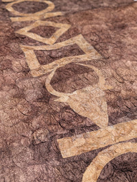 A close-up of a textured brown wild silk tapestry featuring a large, stylized beige geometric and organic pattern running diagonally across the surface.