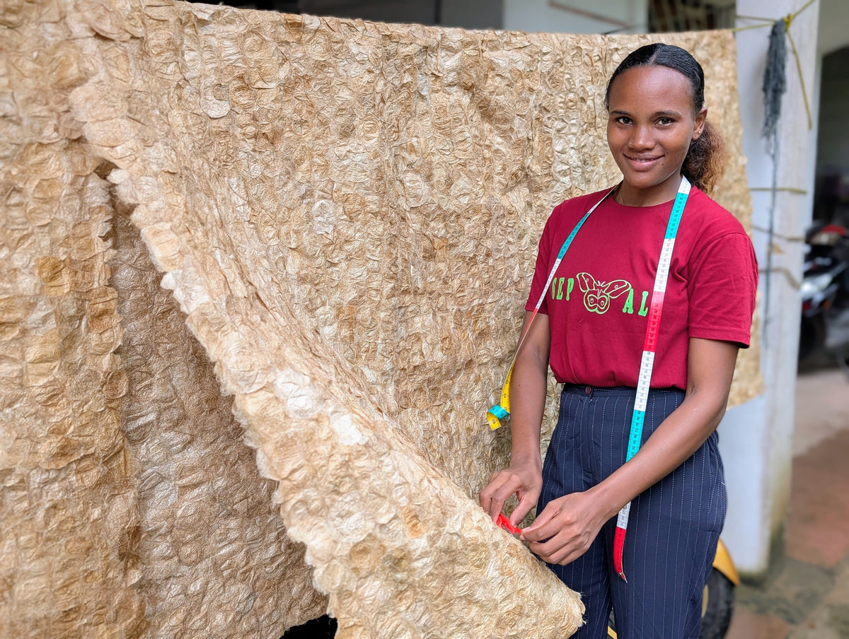 A Tanana Madagascar wild silk artisan stands next to a large handcrafted Ceranchia textile. 