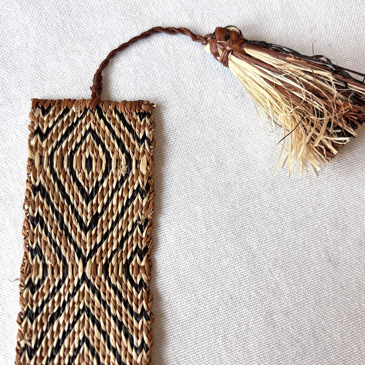 Closeup of handwoven raffia bookmark with pattern of rich brown, black, and light tan. Fair trade, handmade, sustainably sourced raw materials.