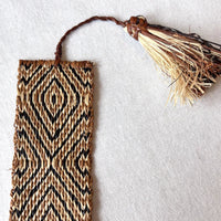 Closeup of handwoven raffia bookmark with pattern of rich brown, black, and light tan. Fair trade, handmade, sustainably sourced raw materials.