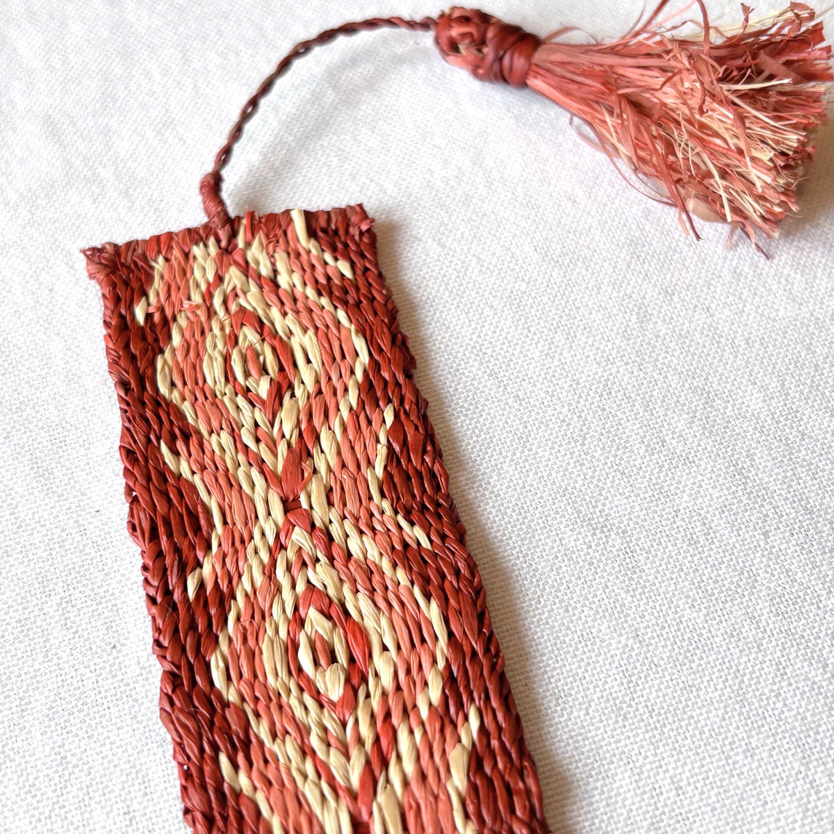 Closeup of handwoven raffia bookmark with pattern of soft egyptian red, light coral, and light tan. Fair trade, handmade, sustainably sourced raw materials.