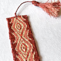 Closeup of handwoven raffia bookmark with pattern of soft egyptian red, light coral, and light tan. Fair trade, handmade, sustainably sourced raw materials.